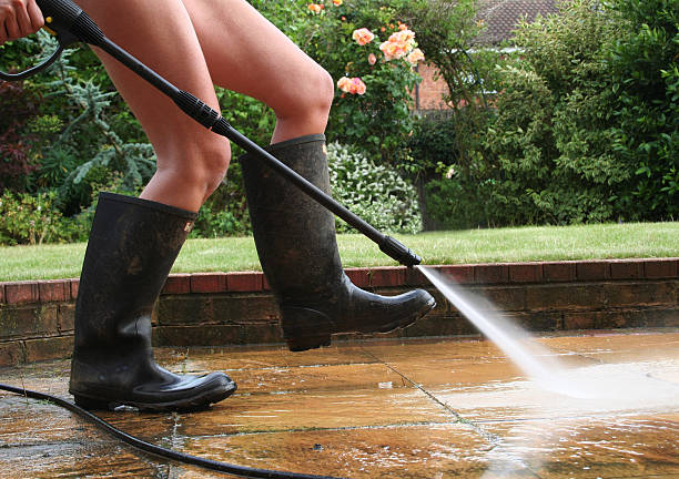 Jeune femme en bottes en caoutchouc qui lave sa terrasse avec un nettoyeur haute pression